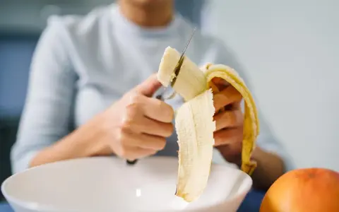 Une personne coupe une banane, riche en potassium, pour prendre soin de son cœur.