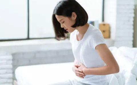 Jeune femme assise sur un lit, se tenant le ventre, souffrant de spasmes intestinaux.