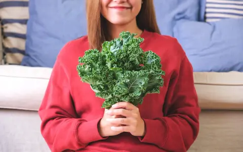 Une femme souriante tient un bouquet de chou kale, un légume aux multiples chou kale bienfaits pour la santé.