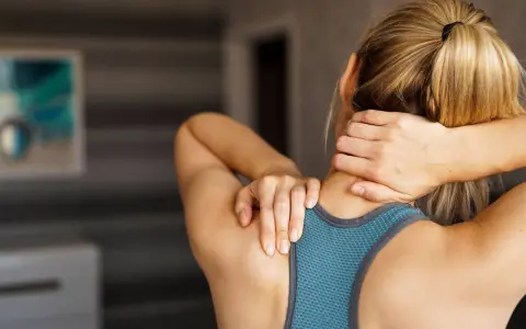 Une femme se masse le cou, cherchant un remède de grand-mère pour sa douleur cervicale.
