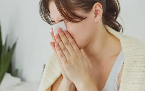 Femme se mouchant avec un mouchoir, cherchant des solutions pour comment arrêter le nez qui coule naturellement.