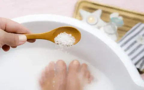 Une cuillère en bois déverse des cristaux dans un bain de pied, pour un moment de détente et de soin.
