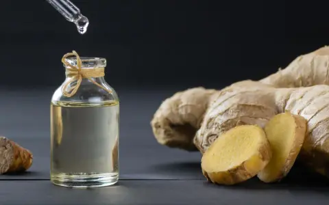 Goutte d'huile essentielle de gingembre aphrodisiaque tombant dans un flacon, à côté de racines de gingembre fraîches.