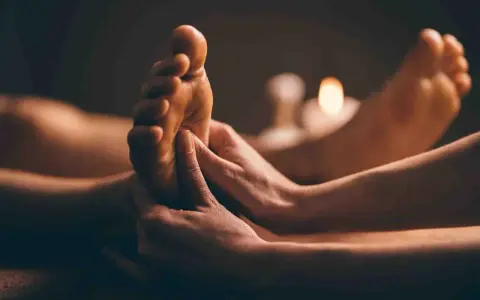 Mains massant un pied, avec des bougies allumées en arrière-plan.