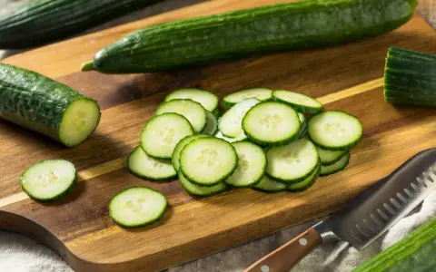 Concombres frais tranchés sur une planche à découper en bois, prêts à révéler leurs nombreux concombre bienfaits. Un couteau est à proximité.