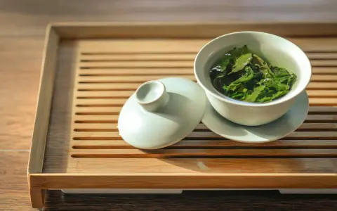 Une tasse de thé vert infusé, prête à révéler ses bienfaits. Le couvercle repose à côté, sur un plateau en bambou.