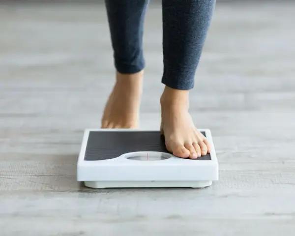 Pieds nus sur une balance, une personne s'interroge sur sa perte de poids inexpliquée.