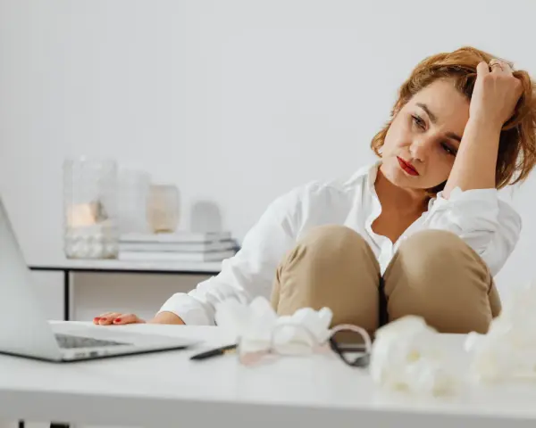 Femme fatiguée, la main dans les cheveux, le regard perdu. Elle semble souffrir de carence en fer et d'anxiété, accablée par le travail.