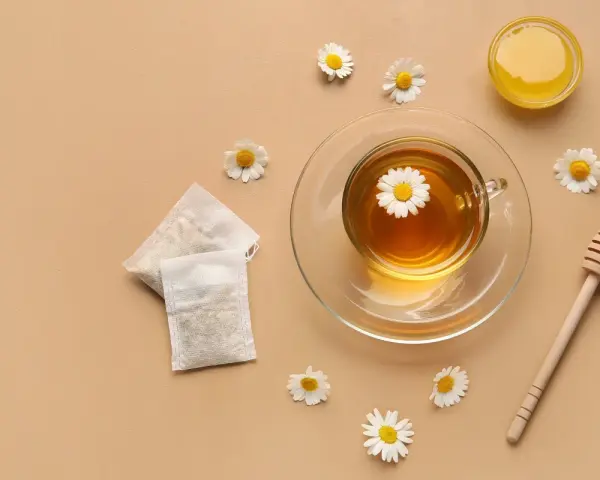 Une tasse de tisane pour le rhume et la toux, avec des sachets, du miel et des fleurs de camomille.
