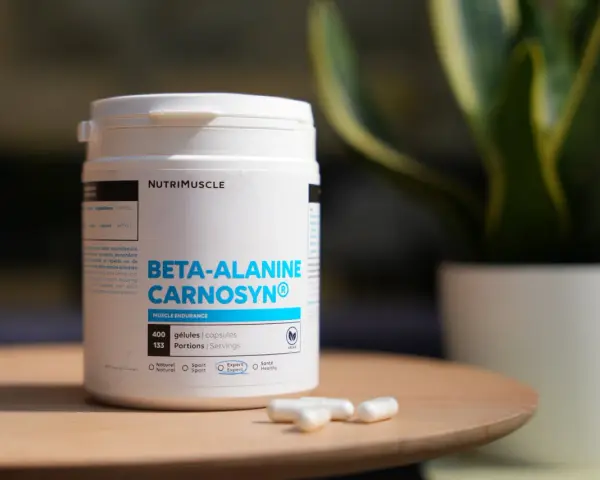 Bouteille de bêta-alanine Carnosyn® pour l'endurance musculaire, avec des capsules sur une table en bois.