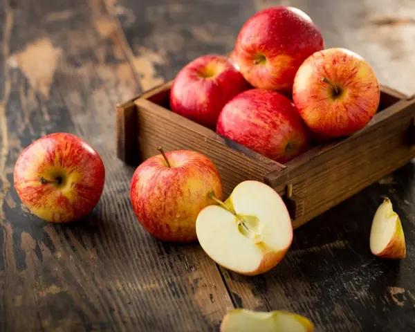 Des pommes rouges et jaunes dans une caisse en bois sur une table rustique. Une pomme est coupée en deux, révélant sa chair blanche. Ces fruits sont un concentré de pomme bienfaits.