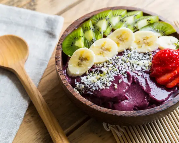 Un bol de smoothie aux fruits d'açaï, garni de bananes, de kiwis, de fraises et de graines.