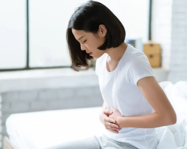 Jeune femme assise sur un lit, se tenant le ventre, souffrant de spasmes intestinaux.