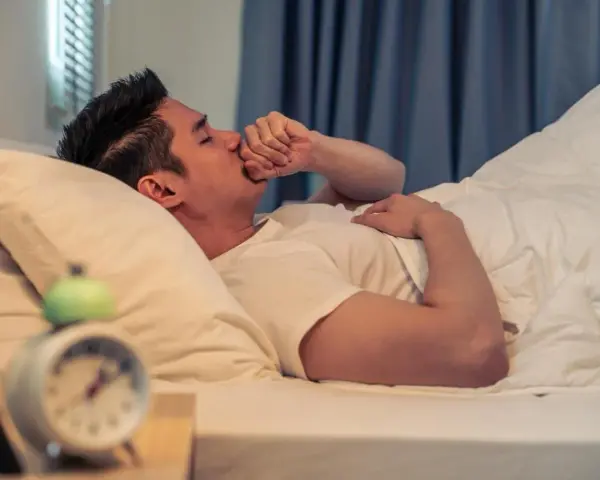 Un homme se réveille en pleine nuit, la main sur la bouche, pris d'une toux nocturne. L'horloge sur la table de nuit indique qu'il est 3h du matin.