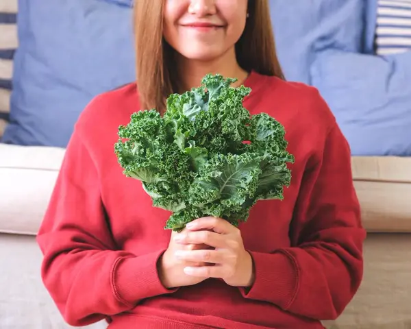Une femme souriante tient un bouquet de chou kale, un légume aux multiples chou kale bienfaits pour la santé.