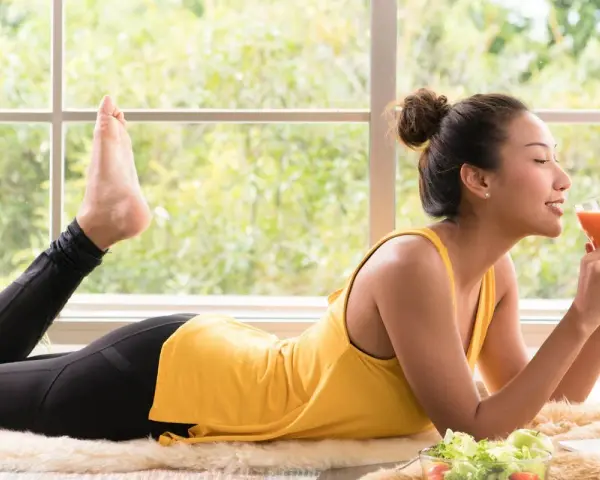 Femme en tenue de sport savourant un jus, pensant au detox foie combien de temps. Salade et ordinateur à proximité.