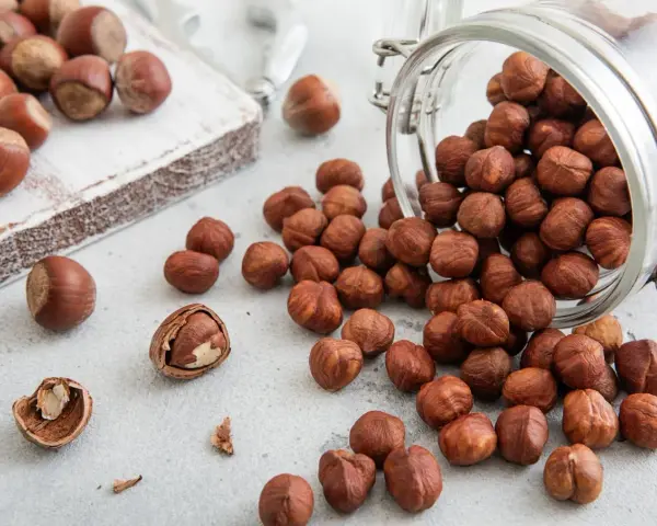 Des noisettes bienfaits : une poignée de ces fruits secs, certains dans un bocal renversé, d'autres sur une planche en bois, promettent une alimentation saine.
