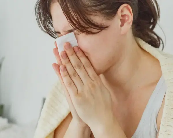 Femme se mouchant avec un mouchoir, cherchant des solutions pour comment arrêter le nez qui coule naturellement.