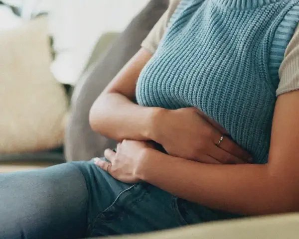Une personne assise sur un canapé, tenant son abdomen, suggérant où se situe une douleur au foie.