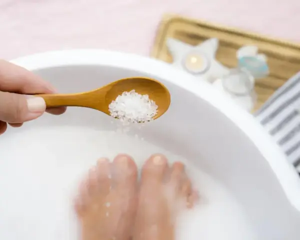 Une cuillère en bois déverse des cristaux dans un bain de pied, pour un moment de détente et de soin.