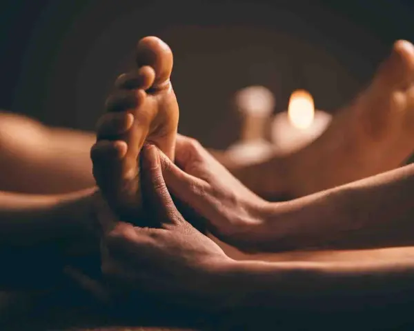 Mains massant un pied, avec des bougies allumées en arrière-plan.
