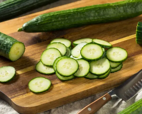 Concombres frais tranchés sur une planche à découper en bois, prêts à révéler leurs nombreux concombre bienfaits. Un couteau est à proximité.