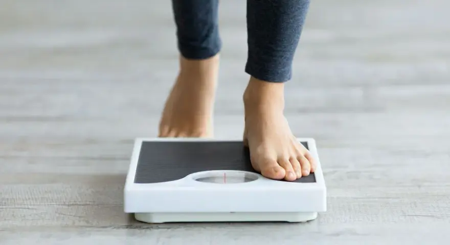 Pieds nus sur une balance, une personne s'interroge sur sa perte de poids inexpliquée.