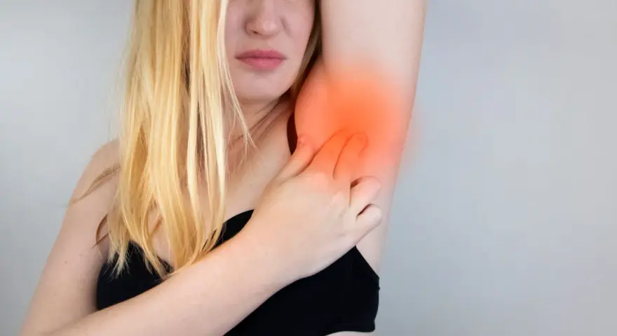 Une femme blonde exprime une douleur vive à l'aisselle, se tenant le bras avec une expression de souffrance.