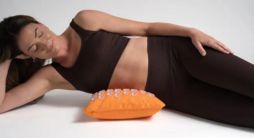Femme détendue sur un coussin d'acupression orange, une solution pour le mal de hanche que faire.