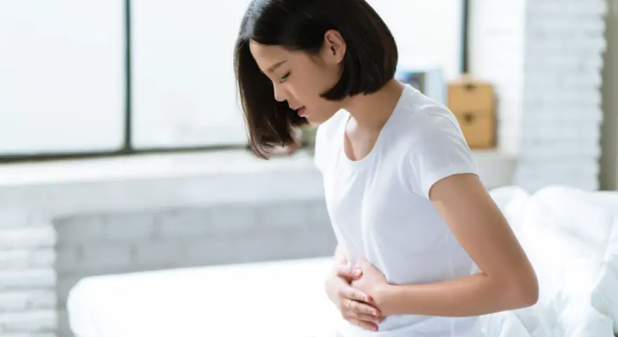 Jeune femme assise sur un lit, se tenant le ventre, souffrant de spasmes intestinaux.