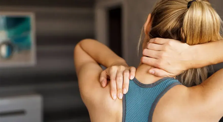 Une femme se masse le cou, cherchant un remède de grand-mère pour sa douleur cervicale.