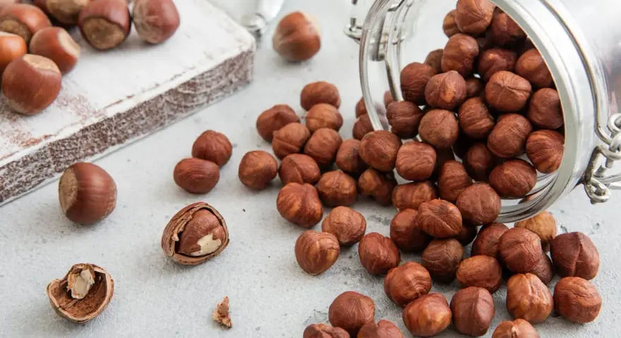 Des noisettes bienfaits : une poignée de ces fruits secs, certains dans un bocal renversé, d'autres sur une planche en bois, promettent une alimentation saine.