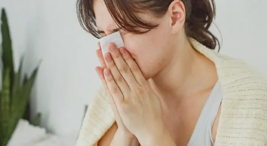 Femme se mouchant avec un mouchoir, cherchant des solutions pour comment arrêter le nez qui coule naturellement.