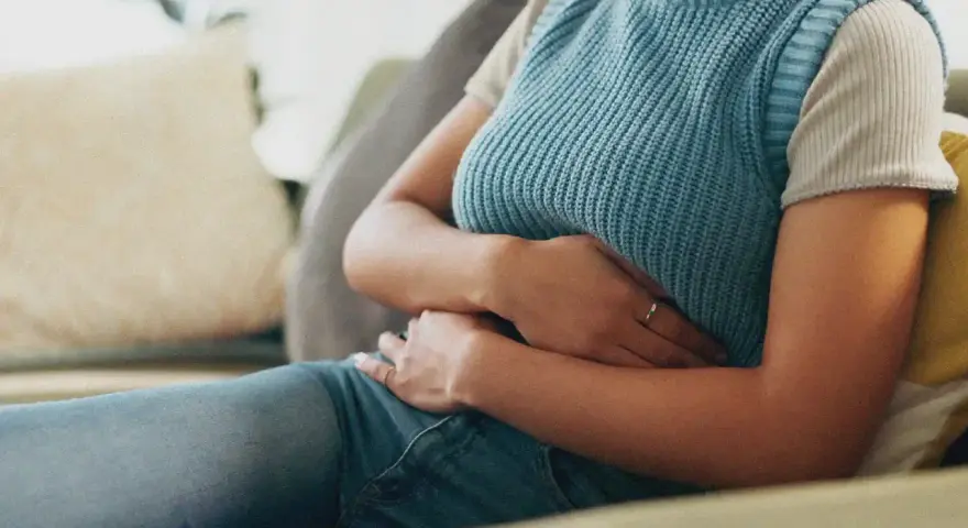 Une personne assise sur un canapé, tenant son abdomen, suggérant où se situe une douleur au foie.