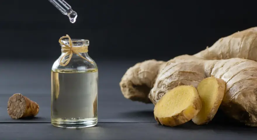 Goutte d'huile essentielle de gingembre aphrodisiaque tombant dans un flacon, à côté de racines de gingembre fraîches.