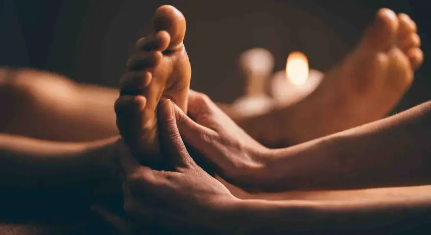 Mains massant un pied, avec des bougies allumées en arrière-plan.