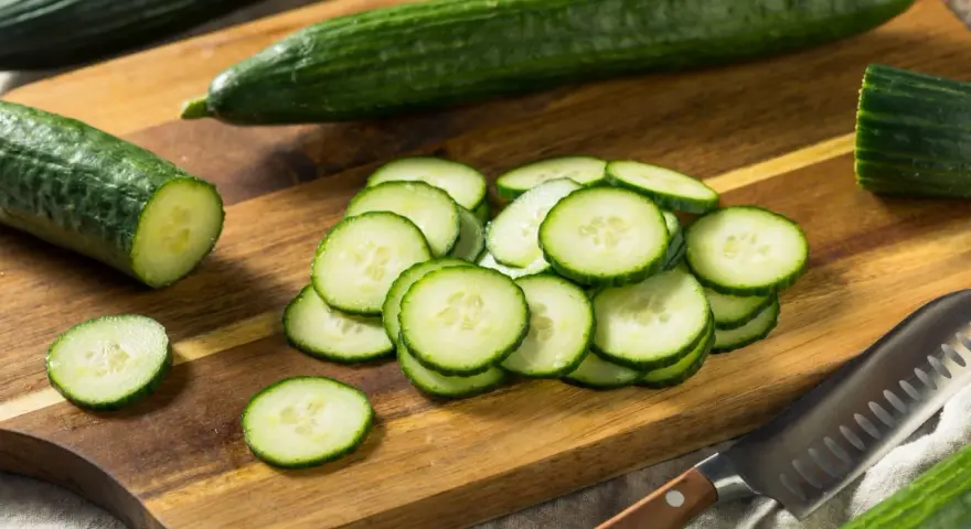 Concombres frais tranchés sur une planche à découper en bois, prêts à révéler leurs nombreux concombre bienfaits. Un couteau est à proximité.