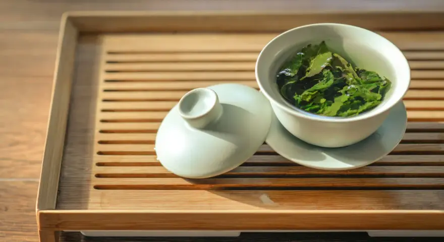 Une tasse de thé vert infusé, prête à révéler ses bienfaits. Le couvercle repose à côté, sur un plateau en bambou.