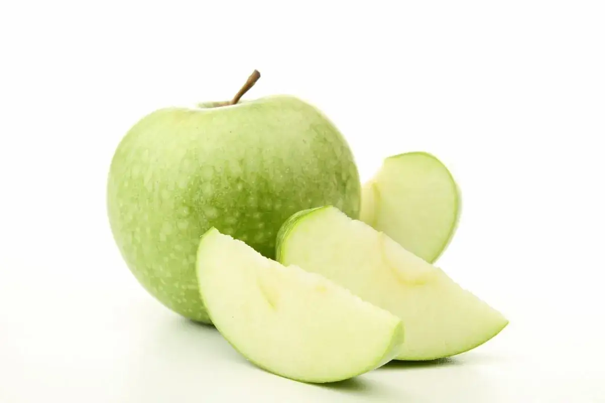 Une pomme verte entière et trois quartiers de pomme verte sur fond blanc.