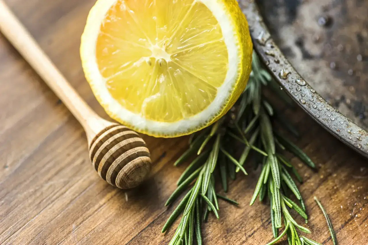 Une tranche de citron, du romarin frais et une cuill&egrave;re en bois sur une planche. Pr&eacute;parer une infusion romarin citron bienfaits pour la sant&eacute;.