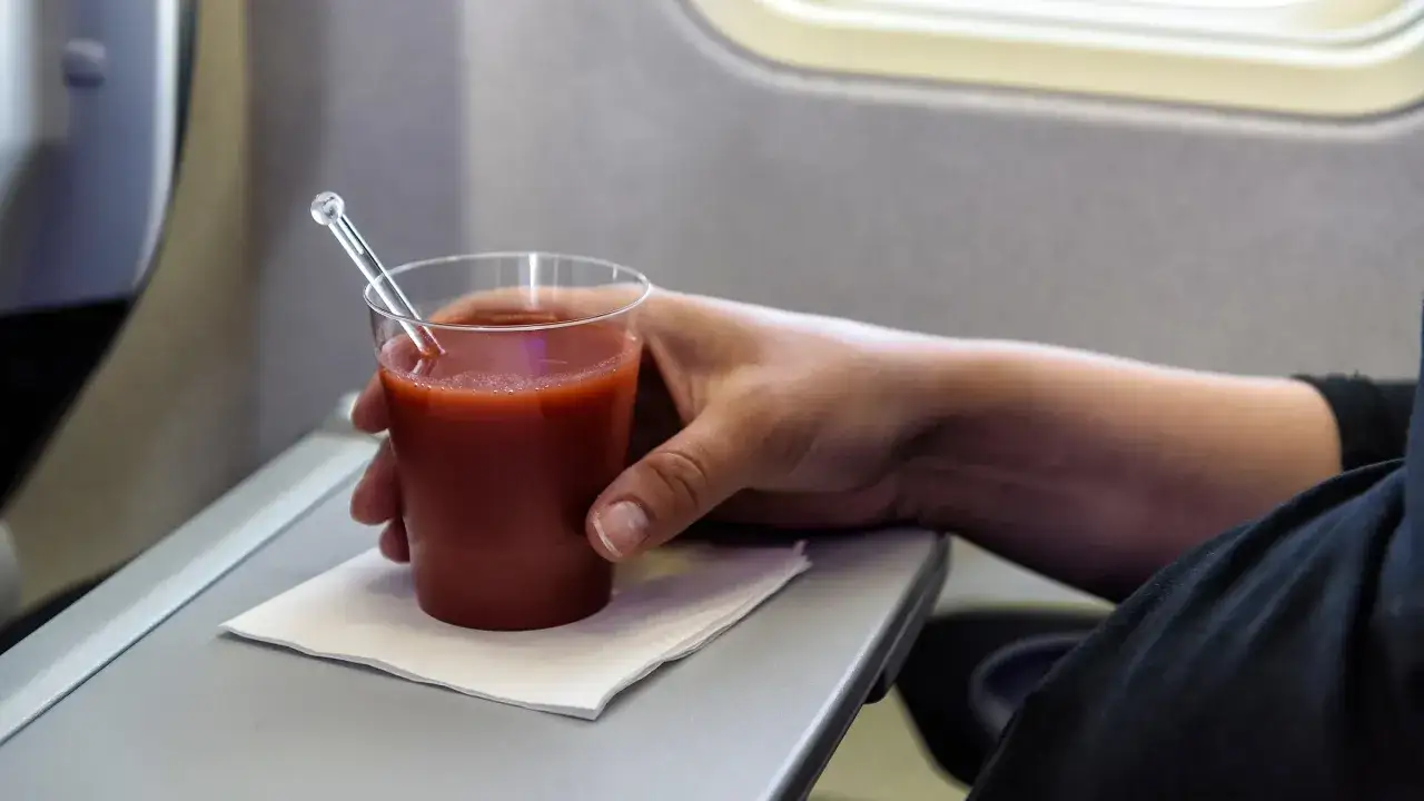 Main tenant une tasse de jus de tomate sur un plateau d'avion.