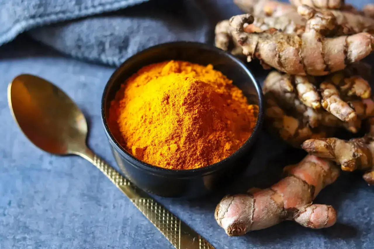Poudre de curcuma dans un bol, &agrave; c&ocirc;t&eacute; de racines de curcuma et d'une cuill&egrave;re dor&eacute;e. Attention au curcuma danger potentiel.