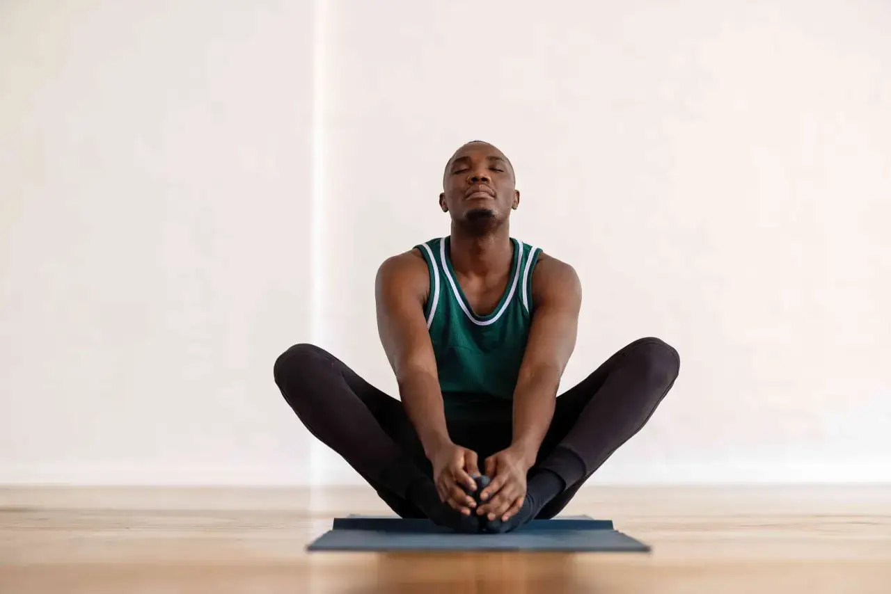 Un homme en tenue de sport, yeux fermés, mains sur les pieds, dans une position pour évacuer les gaz intestinaux.