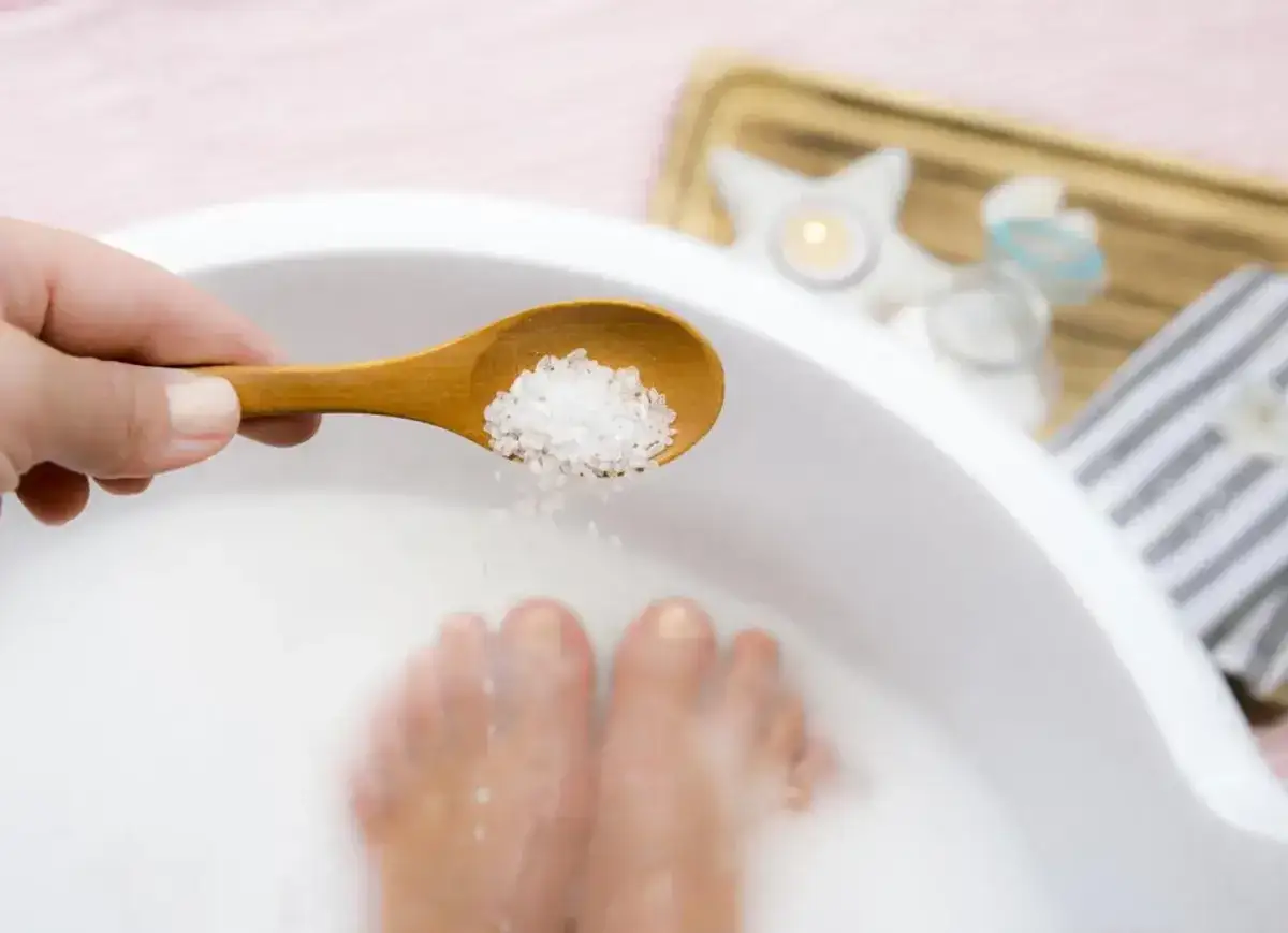 Une cuill&egrave;re en bois d&eacute;verse des cristaux dans un bain de pied, pour un moment de d&eacute;tente et de soin.