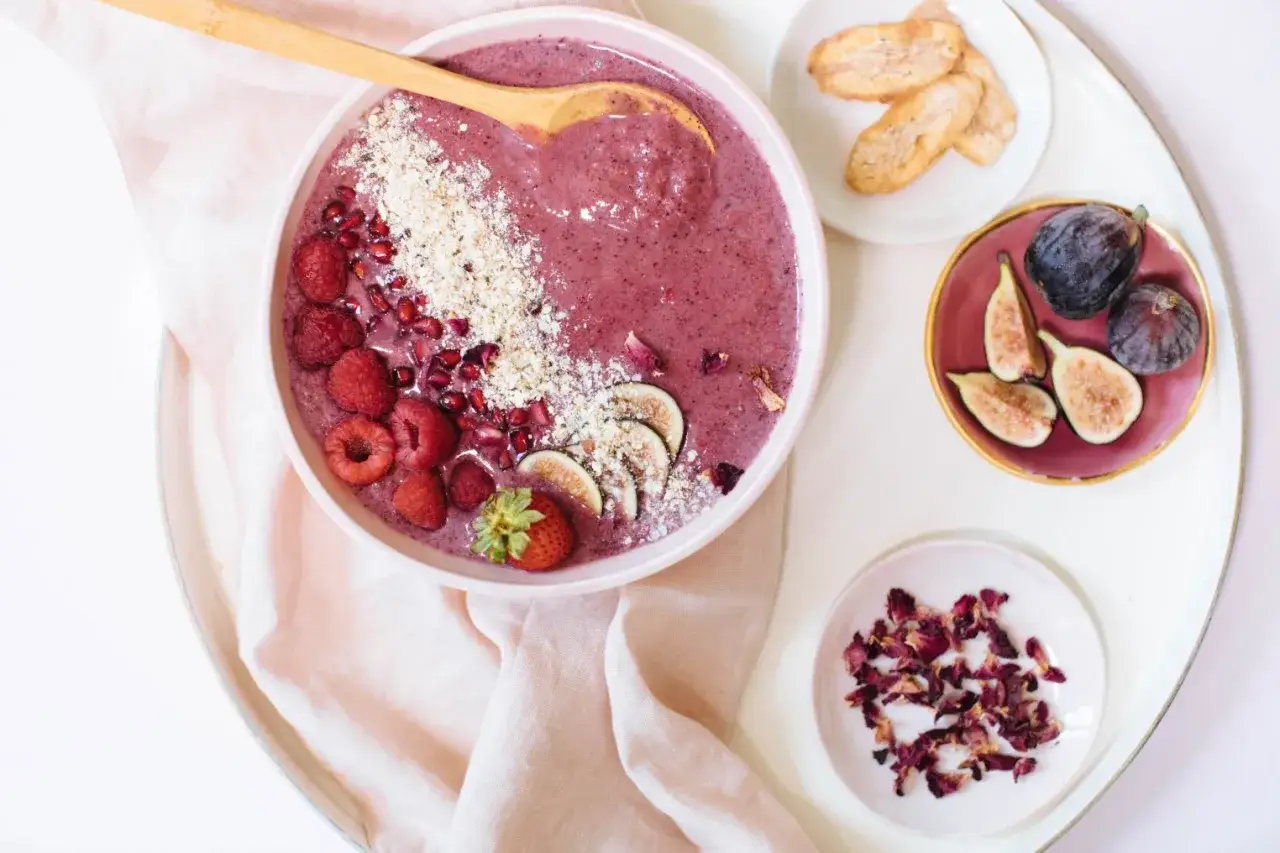 Un bol de smoothie aux baies d'a&ccedil;a&iuml;, garni de framboises, grenade, figues et granola. Servi avec des figues fra&icirc;ches et des p&eacute;tales de rose.
