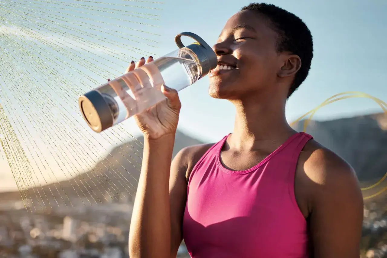 Une femme boit de l'eau pour détoxifier son corps, profitant du soleil et de la nature.