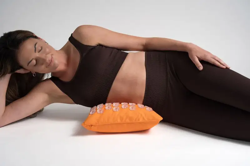 Femme détendue sur un coussin d'acupression orange, une solution pour le mal de hanche que faire.
