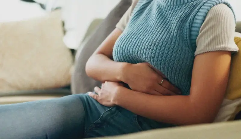 Une personne assise sur un canapé, tenant son abdomen, suggérant où se situe une douleur au foie.